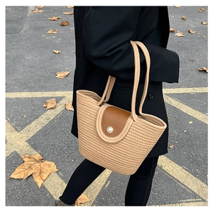 Detail of woven straw tote bag featuring a leather flap and large pearl button closure