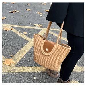 Detail of woven straw tote bag with brown leather flap and pearl accent in autumn street setting