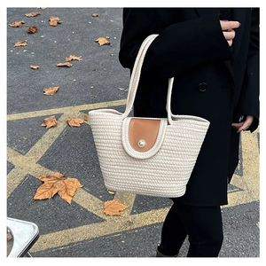 Detail of cream woven tote bag featuring brown leather flap and pearl buckle accent