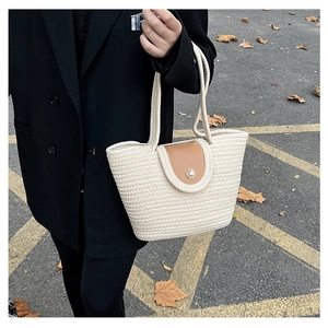 Detail of woven straw bucket bag with brown leather flap and pearl closure accent
