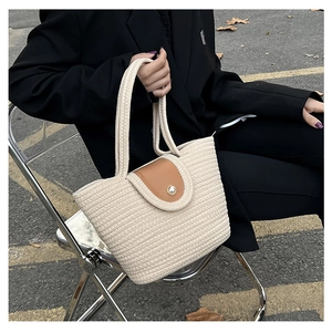 Detail of woven straw tote bag featuring brown leather flap and pearl buckle closure