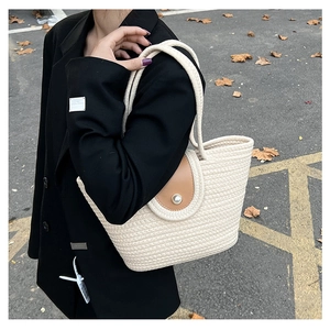 Close-up of cream woven bucket bag with leather flap and pearl clasp on model