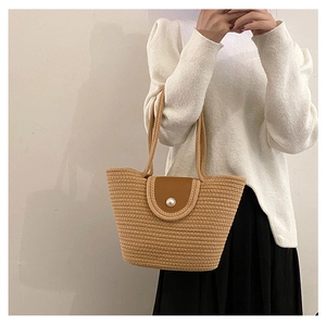 Detail of woven straw bucket bag featuring a brown faux leather flap and pearl accent