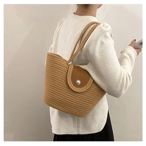 Detail of woven straw handbag featuring a leather flap and pearl closure for women
