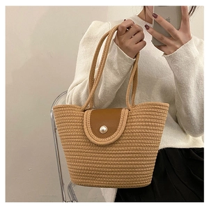 Detail of woven straw handbag with brown leather flap and large pearl button closure