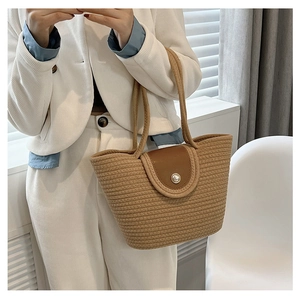 Detail of woven straw tote bag featuring a leather flap and elegant pearl closure