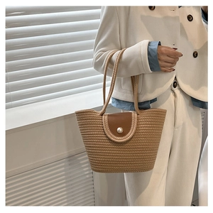 Close-up of woven bucket bag with brown leather flap and pearl clasp detail