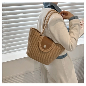 Detail of woven straw basket bag featuring brown leather flap and large pearl buckle closure
