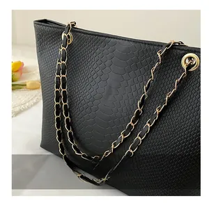 Detail of black faux-crocodile tote bag with gold metal chain and leather braided strap