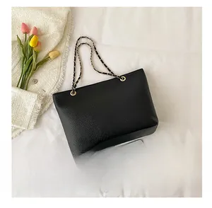Detail of black faux snake leather tote bag with gold chain strap next to a tablet