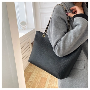 Detail of black crocodile texture tote bag with gold chain strap on model shoulder