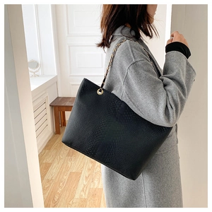 Close-up of elegant black crocodile pattern tote bag with golden metal chain strap detail