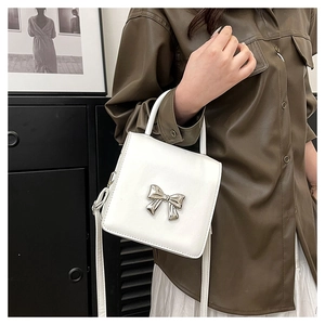 Detail of white square crossbody bag featuring a silver metal bow and adjustable strap