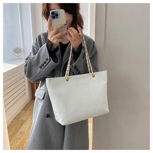 White crocodile pattern tote bag with gold chain straps shown on grey wool coat