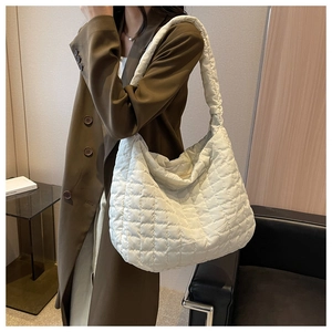 Detail of a white quilted tote bag in soft nylon fabric worn with a brown coat