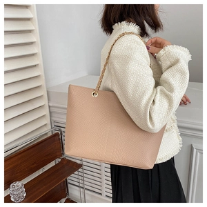 Detail of pink croc-embossed tote bag featuring a gold metal chain and leather shoulder strap