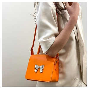 Close-up of orange mini crossbody bag featuring a silver metal bow detail and handle