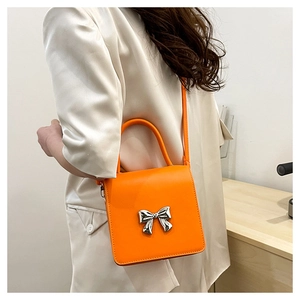 Detail view of a bright orange crossbody bag featuring a silver bow metal clasp detail