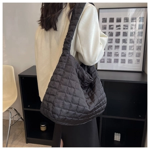 Detail of black quilted puffer tote bag with square stitching and wide shoulder strap