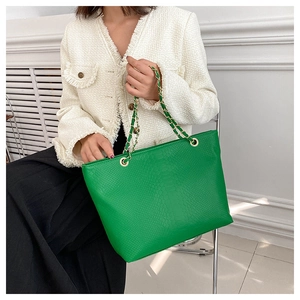 Detail of green tote bag with snake skin pattern texture and golden chain strap
