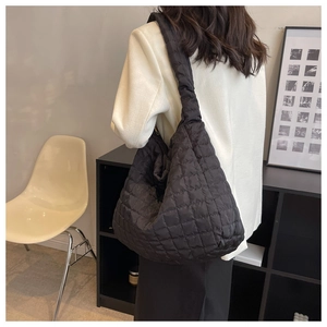 Rear view of a black quilted puffer tote bag shown on model in a minimalist setting