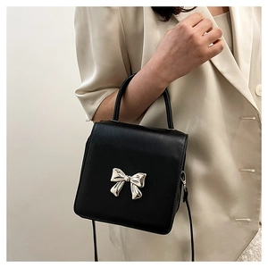 Macro detail of black crossbody bag with silver bow buckle and elegant top handle
