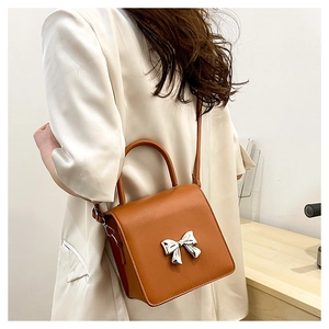 Detail of brown leather shoulder bag with a silver bow metal buckle on a model