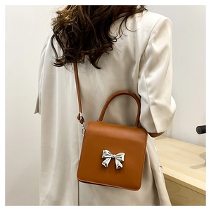 Brown square crossbody bag with silver metal bow worn by a model in a minimalist setting