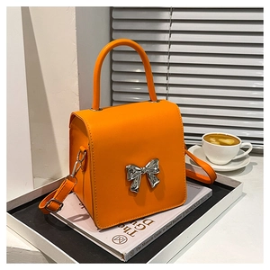 Detail of orange leather crossbody bag with silver bow buckle on white background