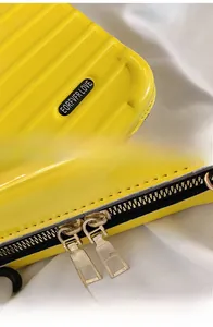 Detail of yellow hardshell mini suitcase bag with metal logo and dual golden zippers