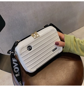 Detailed view of mini white suitcase-style crossbody bag with wide lettered strap