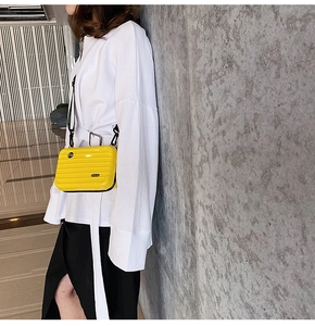 Detail of yellow mini suitcase crossbody bag with grooved texture on a model