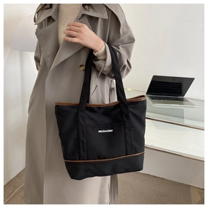 Détail du sac cabas en toile noire avec garniture en cuir brun porté à l'épaule