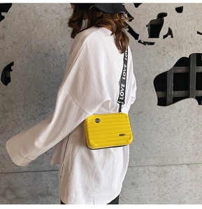Close-up of a bright yellow mini suitcase crossbody bag with a branded LOVE strap