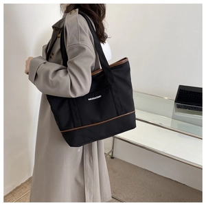 Détail du sac cabas en toile noire avec garniture en cuir marron et doubles poignées