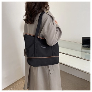 Détail du sac cabas en toile noire avec bordure en cuir marron porté par un mannequin