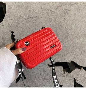 Close-up of a red mini suitcase-shaped crossbody bag with a wide striped nylon shoulder strap
