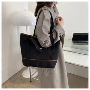 Détail d'un sac cabas en toile noire avec garniture en cuir marron et large bandoulière