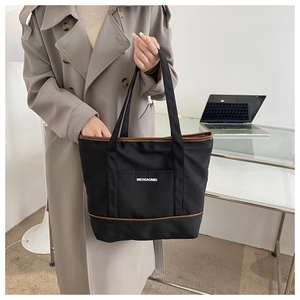 Vue détaillée du sac cabas noir avec bordure marron et logo porté avec un trench-coat