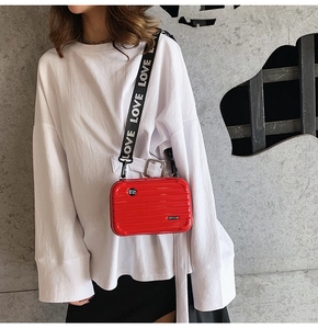 Detail of red mini suitcase crossbody bag with logo badge and LOVE letter strap