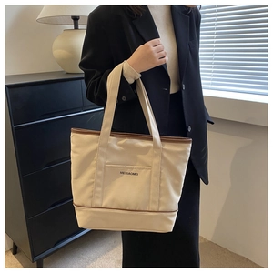 Détail du sac cabas en toile beige avec bordure en cuir marron et poche frontale