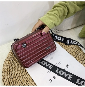 Macro shot of burgundy suitcase-style mini phone bag with wide branded strap