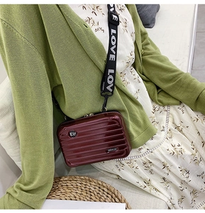 Miniature burgundy suitcase crossbody bag with LOVE strap shown in a lifestyle setting