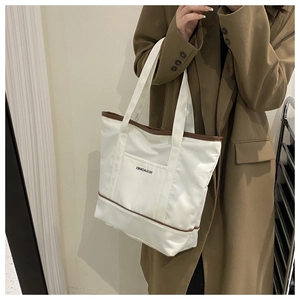 Détail d'un sac cabas en toile blanche avec bordure en cuir marron et poche avant