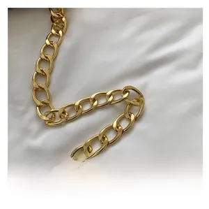 Detailed view of glossy gold metal chain strap on minimalist small square handbag
