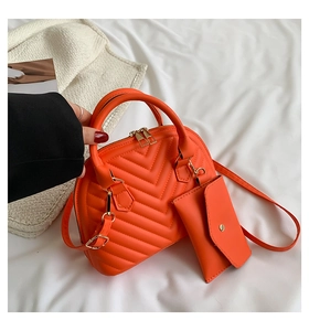 Détail du sac orange avec matelassage en V, pochette assortie et accents dorés brillants