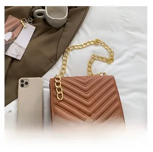 Detail of caramel chevron quilted shoulder bag with chunky gold chain strap on white linen