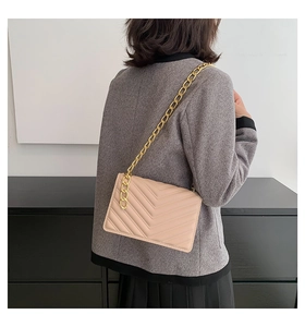 Detail of beige quilted shoulder bag with V-shaped chevron stitching and gold chain