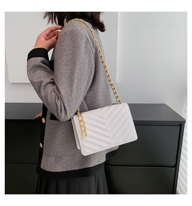 Close-up of white chevron quilted handbag with elegant gold chain strap worn by a model
