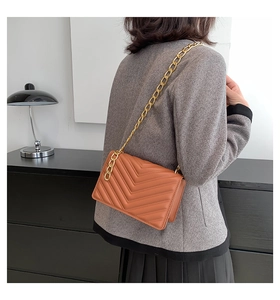 Detail view of a bright orange chevron quilted shoulder bag with gold chain strap